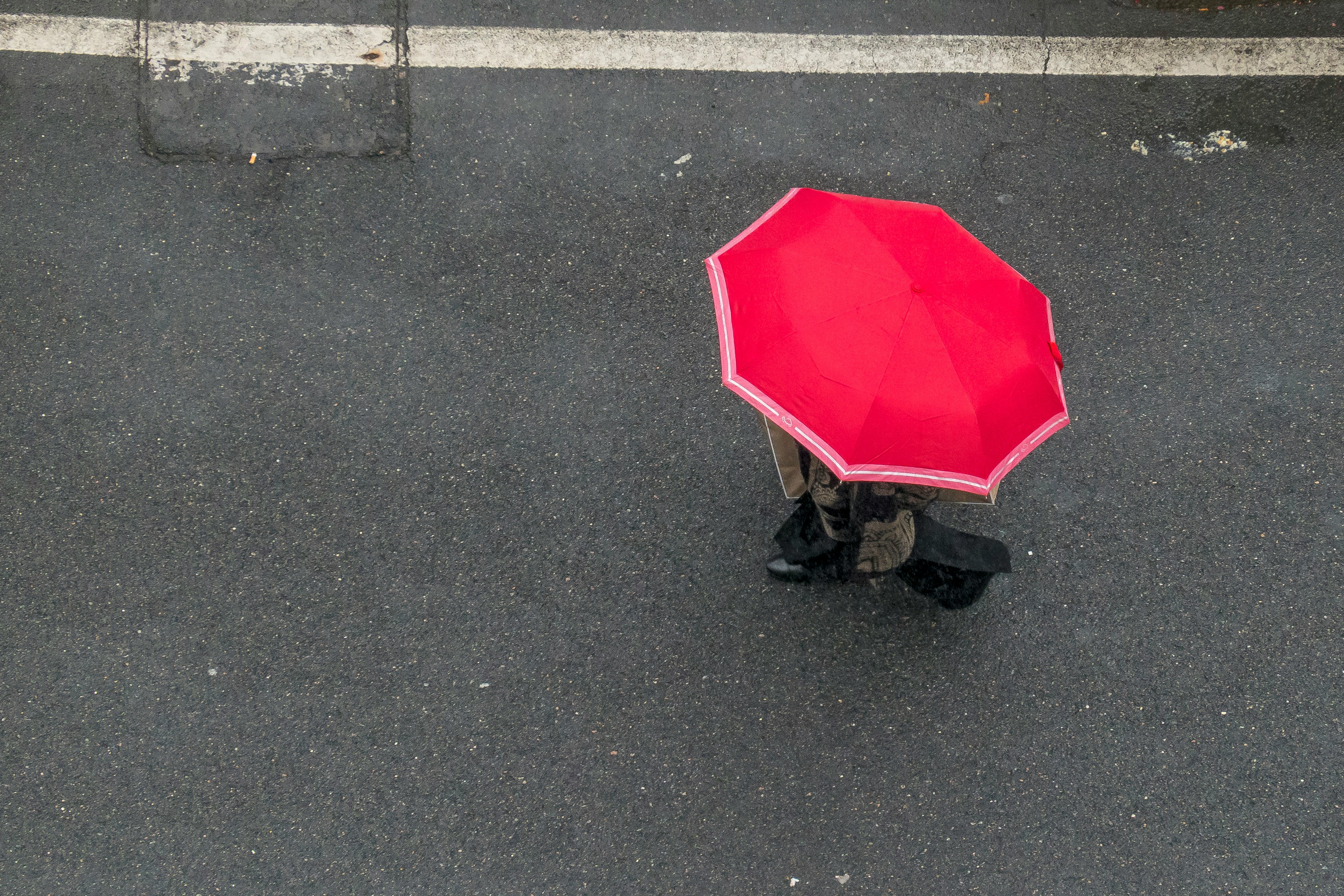 person in red umbrella walking on gray asphalt road during daytime